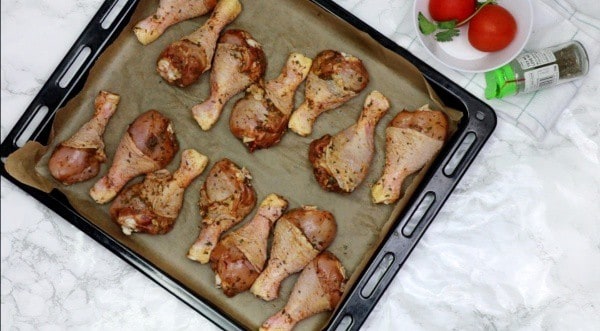 Seasoned chicken arranged on baking paper lined oven tray.