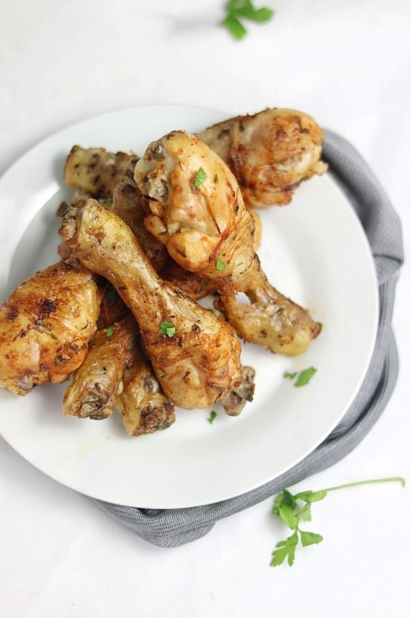 Baked chicken drumsticks piled on one another on a plate.